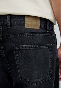 Jeans negru cropped-fit cu o suprafață texturată, dotate cu o etichetă din piele inscripționată "SCALPERS" pe talie și detalii la buzunarul din spate.