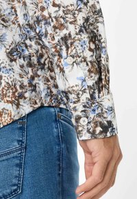 Camicia a maniche lunghe con bottoni, fondo bianco e fantasia floreale in blu e marrone. Tessuto in cotone, maniche lunghe e polsini classici con bottoni.