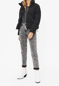 Černá péřová bunda s vysokým límcem, šedé tričko a vybledlé šedé džíny. Bílé kotníkové boty se špičatou špičkou a černým detailem na podpatku.