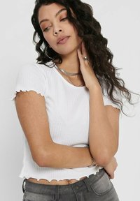 White ribbed crop top with short, wavy sleeves. Features a fitted silhouette and soft texture. Styled with gray high-waisted pants and layered necklaces.