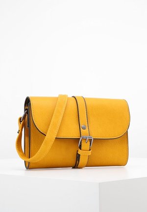 Gul læder crossbody-taske med frontklap, spænde-rem og justerbar skulderrem, der ligger på en hvid overflade.