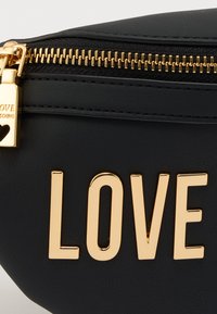 Μαύρο τσαντάκι από συνθετικό δέρμα με χρυστό φερμουάρ και τη λέξη "LOVE" σε γυαλιστερά χρυσά γράμματα. Λείο υλικό με συμπαγή, στρογγυλεμένο σχεδιασμό.