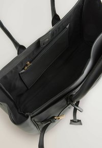 Zwarte leren tote bag met een zachte textuur, gouden ritsvak aan de binnenkant en dubbele handgrepen. Heeft minimale stikdetails en een magnetische sluiting.
