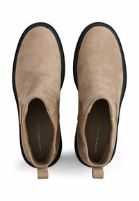 Une paire de bottines en daim beige avec des semelles noires, des panneaux latéraux élastiques et des languettes de tirage, vues de dessus sur un fond blanc.