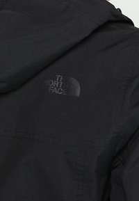 Tissu noir d’une veste présentant un logo « The North Face » embossé subtilement sur la partie supérieure du dos.