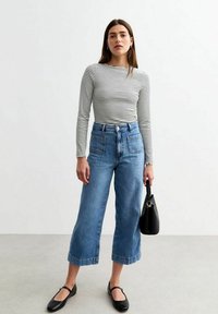 Gestreepte lange mouw top, hooggewaisted wijde jeans van denim, zwarte flats en een zwarte handtas; katoen stof, casual look, neutrale kleuren.
