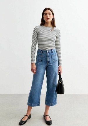 Gestreepte lange mouw top, hooggewaisted wijde jeans van denim, zwarte flats en een zwarte handtas; katoen stof, casual look, neutrale kleuren.