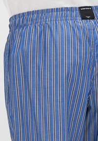 Blauwe en grijs gestreepte stoffen broek met een elastische tailleband en een label met "BJÖRN BORG." Het materiaal lijkt lichtgewicht en zacht te zijn.