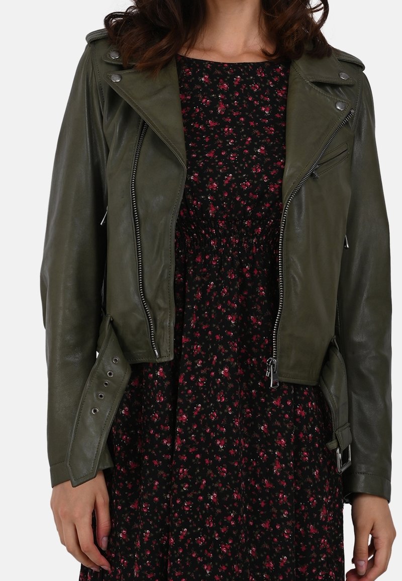 Woman wearing an olive green leather jacket over a black dress with small red floral print, shown from neck to hips.