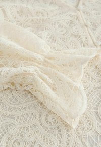 Tissu en dentelle blanche avec des motifs cachemire complexes et des détails délicats et texturés. Matériau doux et léger avec une finition soignée.