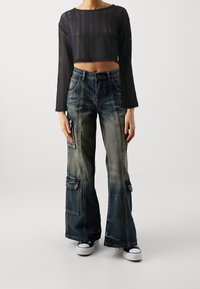 Black cropped mesh top with long sleeves, paired with wide-leg blue denim cargo pants featuring front pockets and a faded wash.