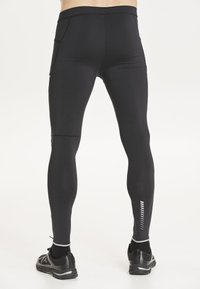 Schwarze Sportleggings mit enganliegendem Schnitt, ausgestattet mit Seitentaschen, reflektierenden Akzenten und einer glatten, dehnbaren Textur.