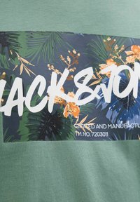 Zelené tričko s tmavým vzorovaným panelem s tropickými listy a květinami, s nápisem "BLACK&JON." Měkká bavlněná látka, design s kulatým výstřihem.