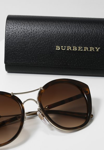 Ochelari de soare Burberry cu lentile degradate maro, rame tortoise negre, accente metalice și un suport din piele întărit cu numele brandului embosat.