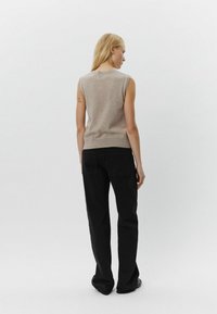 Beige ærmeløs sweater parret med sorte brede bukser. Sweateren har en rund halsudskæring og en tætsiddende form, der fremhæver en glat tekstur.