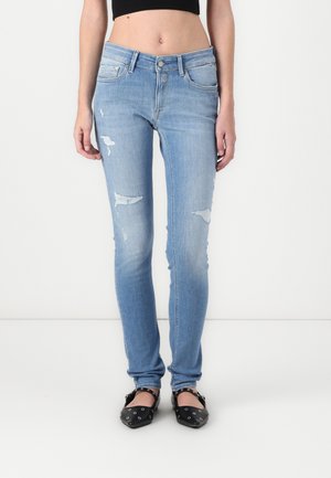 Jeans skinny azzurri chiari con dettagli strappati, vita media e design classico a cinque tasche. Indossati con scarpe flat nere.