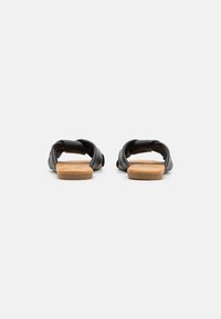 Svart sandal med två tvistade, mjuka remmar och en beige, texturerad fotbädd. Slät yta med en minimalistisk design. Platt sula.