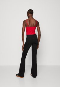 Top rojo de tirantes finos combinado con jeans negros de corte acampanado. Los jeans cuentan con bolsillos traseros y un diseño de cintura alta. Colores sólidos con un detallado mínimo.
