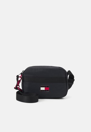 Kleine schwarze Umhängetasche mit verstellbarem Riemen und einem Tommy Jeans Logo-Patch vorne in der Mitte.