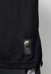 Svart Nike Air-tröja med en texturerad tyg. Har en logotyp och en etikett i vitt som beskriver materialets äkthet och skötselråd.