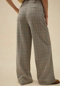 Hochtaillierte, weite Hosen aus leichtem Stoff mit einem karierten Muster in Braun, Schwarz und Creme, die seitliche Taschen besitzen.