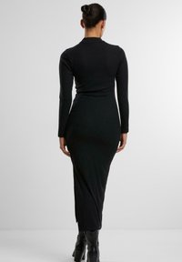 Abito nero a maniche lunghe con scollo alto, dalla silhouette aderente e spacco laterale, realizzato in un tessuto elastico.