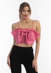 Roze satijnen crop top met een grote strik in het midden, voorzien van dunne bandjes. Gecombineerd met zwarte aansluitende broek voor contrast.