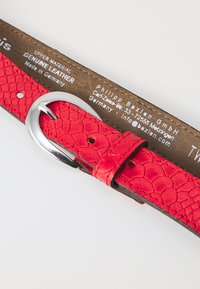 Röd äkta läderbälte med ett texturerat reptilmönster, silverfärgad metallspänne och en brun läderinredning med varumärkesinformation.