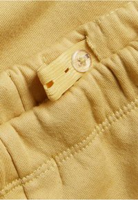 Gult tyg med knappstängning och rynkad struktur, med synliga sömnadsdetaljer och en mjuk, slät yta.