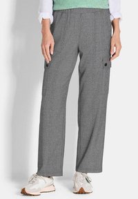 Graue, weit geschnittene Cargo-Hosen aus strukturiertem Stoff, mit Seitentaschen und Knöpfen. Getragen mit weißen Sneakern und einem grünen Pullover.