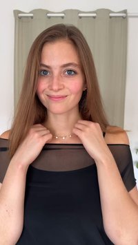 Fekete, áttetsző felső váll nélküli kivágással. Arany nyaklánc kis kör alakú díszítésekkel. Hosszú barna haj és természetes fényben látható bőrtónusok.