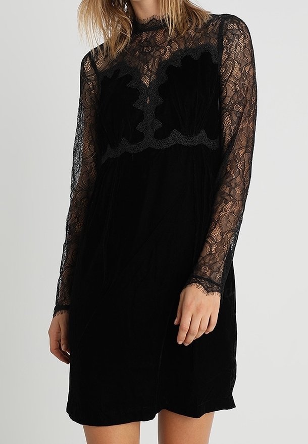 Robe noire avec un corsage en velours texturé et des manches longues en dentelle. Présente un design en dentelle festonné au niveau de la poitrine et une coupe décontractée.