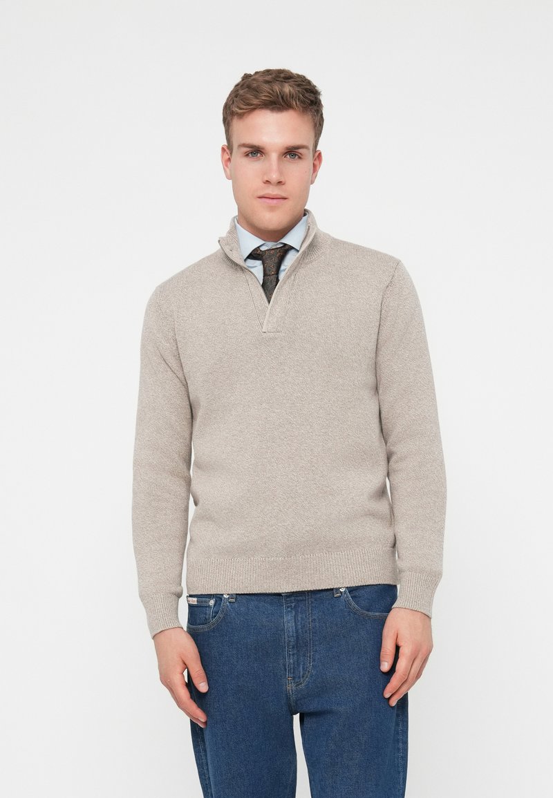 Jasno beżowy sweter dzianinowy z kołnierzem na ćwierć suwaka, ściągaczami na r�ękawach i u dołu. Nosi się go na niebieskiej koszuli oraz w połączeniu z dżinsami w kolorze niebieskim.