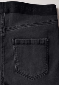 Svarta denimjeans med en slät textur, med en bakficka och ett midjeband präglat med "ONE DENIM" och "STR."