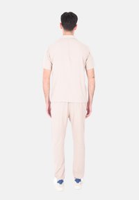 Camicetta beige a maniche corte e pantaloni abbinati realizzati in materiale morbido e leggero. L'outfit presenta una vestibilità rilassata e un design minimal.