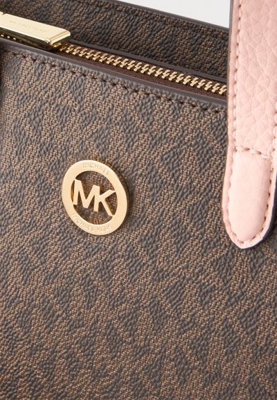 Καφέ υφασμάτινη τσάντα Michael Kors με χρυστό κυκλικό λογότυπο, χρυστό φερμουάρ και ροζ δερμάτινο λουρί ορατό στη δεξιά πλευρά.