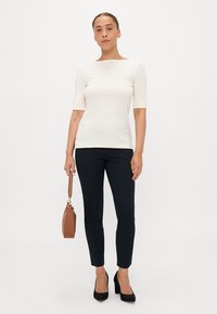 Tej fehér, rövid ujjú felső sötétkék, slim-fit nadrággal kombinálva, fekete hegyes orrú magassarkúval és barna táskával. Egyszerű, testhezálló dizájn, sima textúra.