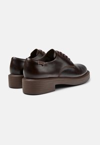 Chaussures en cuir marron avec une finition lisse, bout rond et une semelle en caoutchouc marron texturé et basse. Comprend des lacets et une petite étiquette de marque sur le talon.