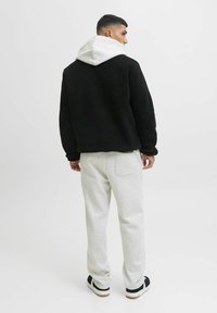 Giacca in pile nera con cappuccio grigio, abbinata a pantaloni in felpa grigio chiaro. Caratteristiche includono una vestibilità comoda e un materiale testurizzato.