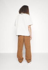 Vit kortärmad skjorta med rak skärning, kombinerad med bruna cargobyxor med fickor, bärs med vita och svarta sneakers.