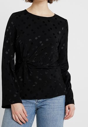 Top nero a maniche lunghe con pois texturizzati, caratterizzato da un design frontale attorcigliato e collo rotondo. Realizzato in un tessuto leggero e liscio.