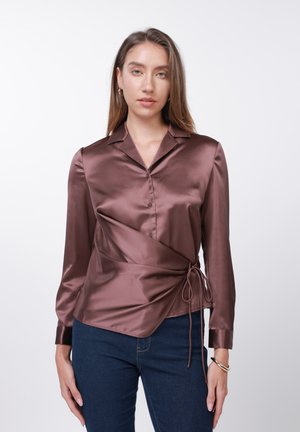 Cămașă satinată în maro intens, cu guler, mâneci lungi, nasturi și detaliu cu legătură laterală. Purtați cu blugi de culoare albastru închis.