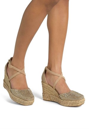 Wedge sandals with a natural woven jute base and beige fabric upper, featuring a diamond-studded toe cap and crisscross ankle straps.