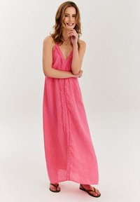 Dlhá ružová ľanová šaty s V-krkom a čipkovým lemom v strede. Šaty sa rozširujú až po členky a majú voľný strih.