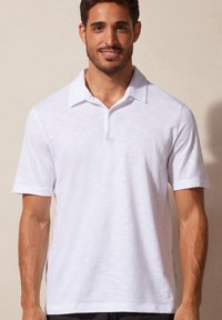 Witte polo shirt van een textuur en lichtgewicht stof. Heeft een klassieke kraag, korte mouwen en een enkele knoopsluiting bij de nek.