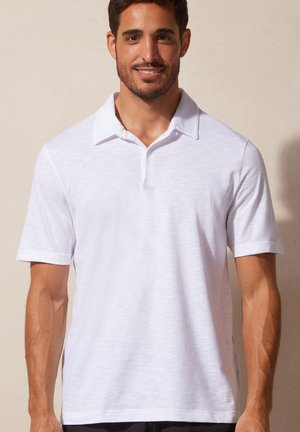 Witte polo shirt van een textuur en lichtgewicht stof. Heeft een klassieke kraag, korte mouwen en een enkele knoopsluiting bij de nek.