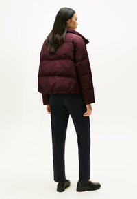Burgundowa kurtka puchowa z wysokim kołnierzem i pikowanym wzorem, w połączeniu z ciemnymi spodniami i czarnymi butami, widok z tyłu.