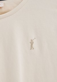 Beige Baumwoll-T-Shirt mit einem kleinen, mit Strass verzierten Golfer-Design auf der linken Brust und einem klassischen Rundhalsausschnitt.