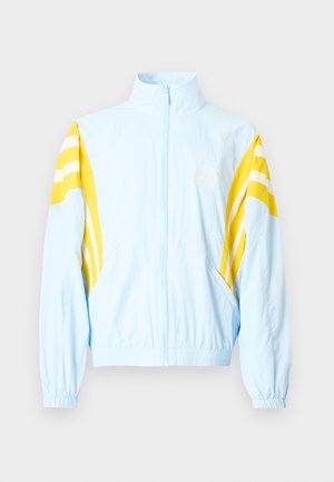 Ανοιχτό μπλε μπουφάν με ψηλό γιακά, κίτρινες διαγώνιες ρίγες στα μανίκια, ελαστικές μανσέτες και φερμουάρ στο μπροστινό μέρος. Διαθέτει λογότυπο στο στήθος.