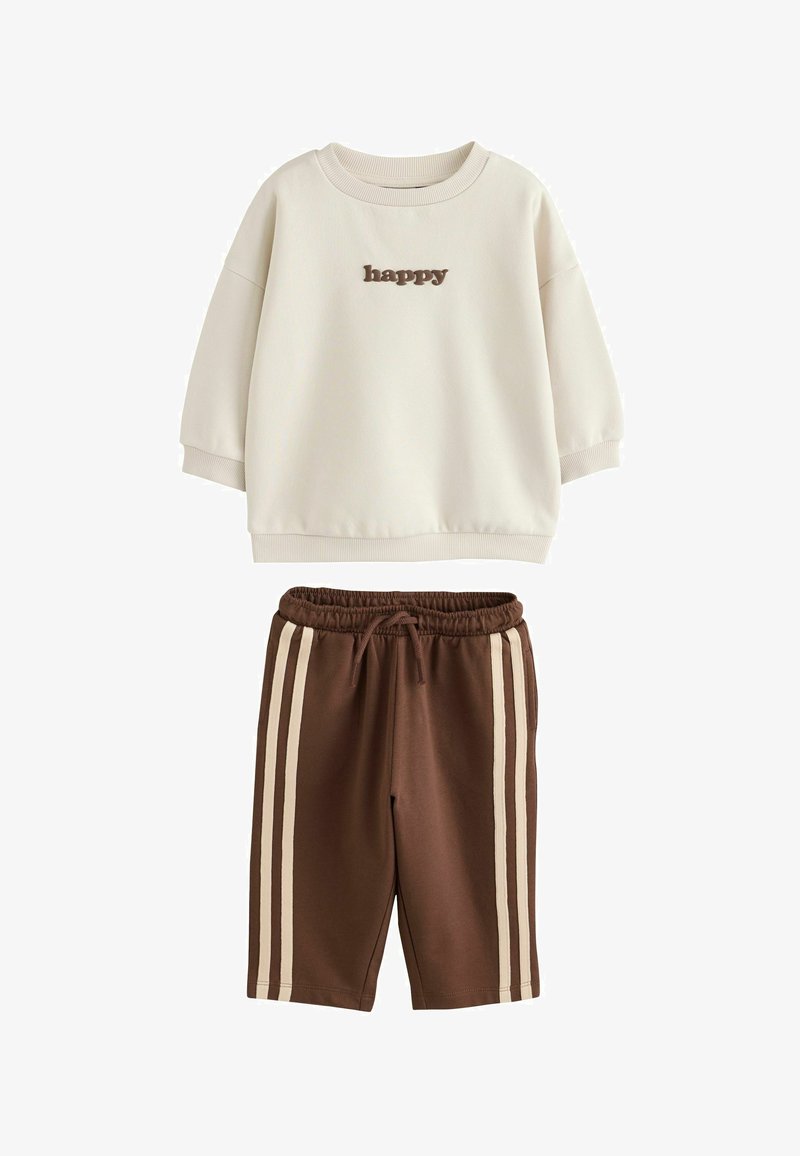 Sudadera crema con texto "happy" en la parte delantera y pantalones cortos marrones con dos franjas laterales beige y cintura con cordón.